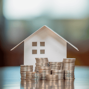 Miniature house with stacked coins representing real estate investment.