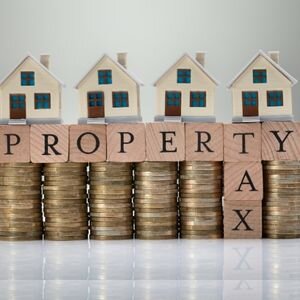 Model houses on stacked coins with property tax blocks for real estate investment.