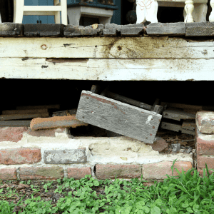 Cracked and damaged foundation under a house with visible brick and wood.