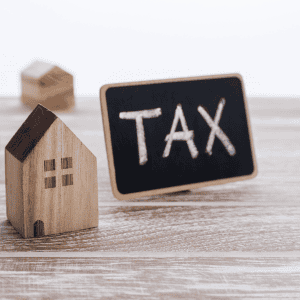 Wooden house model and chalkboard with 'TAX' written on it.
