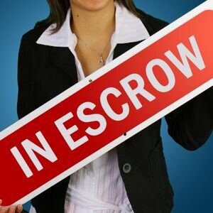 Person holding an 'In Escrow' sign for real estate transaction.