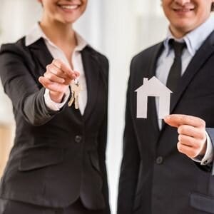 Real estate agents holding house-shaped cutout for home buying.