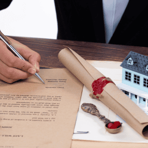 Person signing legal documents for property transfer with house model nearby.