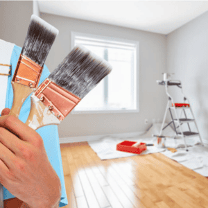 Person holding paintbrushes in a room under renovation.