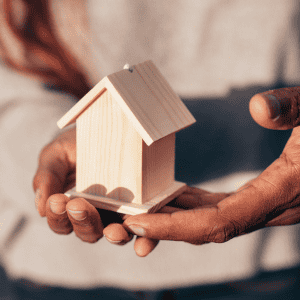 Person holding a small wooden house model for estate planning.