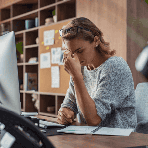 Stressed woman working at desk with computer and notepad.