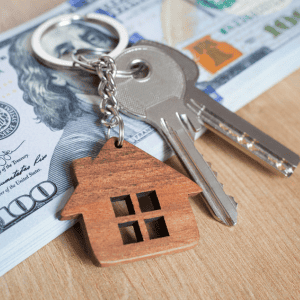 House keys with a wooden house model and cash, symbolizing real estate and home ownership.