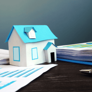 Small paper house, pile of documents and a pen on a table