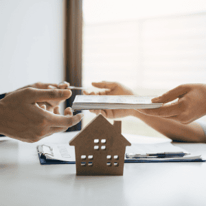 Real estate transaction with hands exchanging documents over a house model.