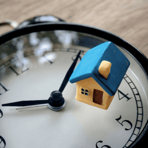 Miniature house on a clock representing real estate timing decisions.