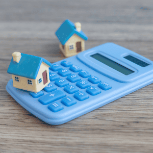 Blue calculator with miniature house models for real estate and financial planning.