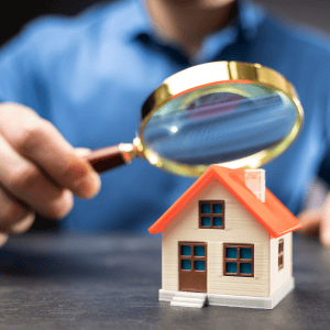 Person examining a house model with a magnifying glass for real estate inspection.