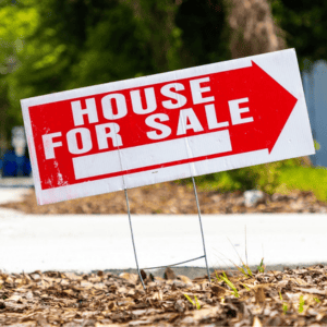 Red and white house for sale sign on lawn with arrow pointing right.